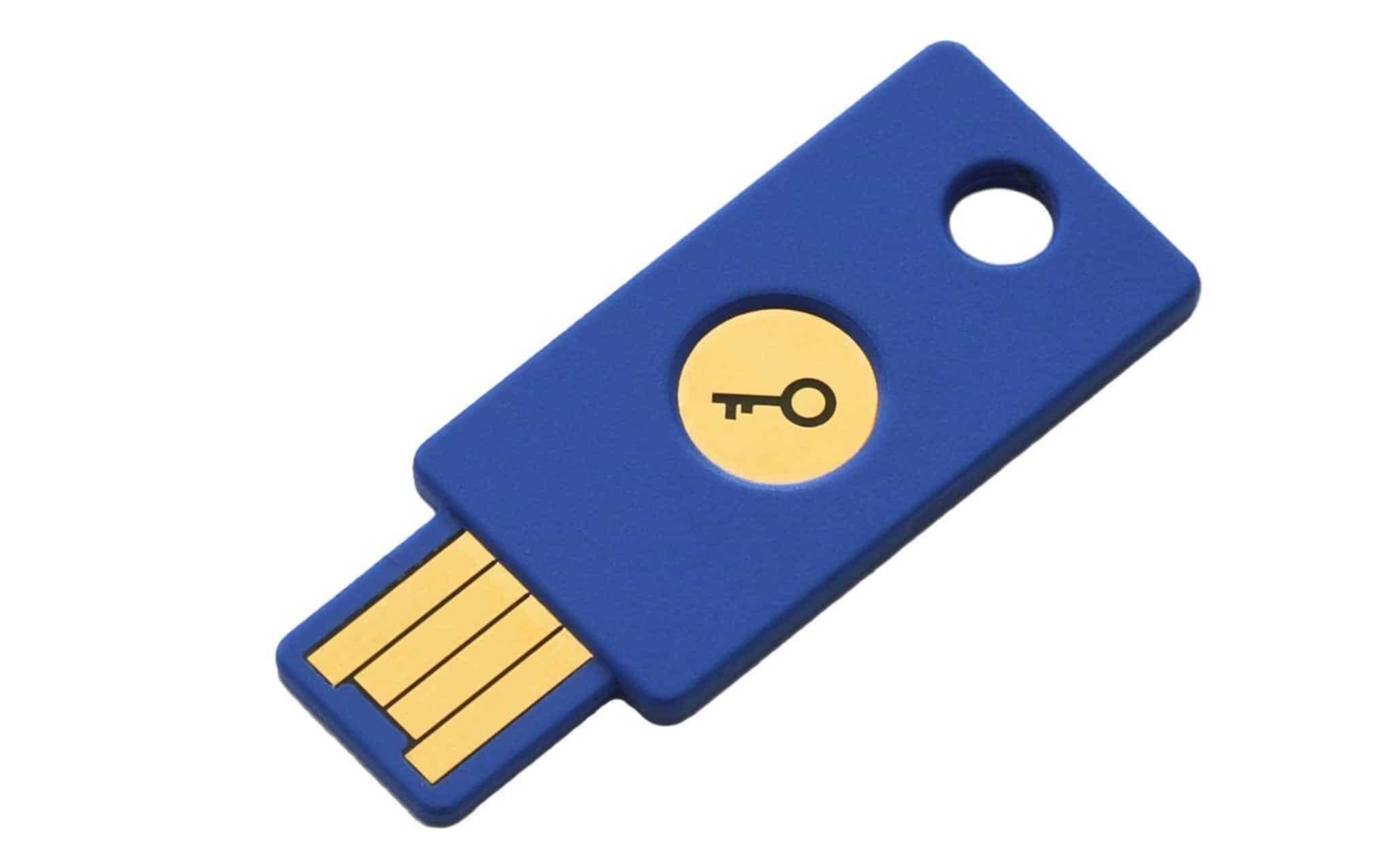A blue USB security key with a gold circular emblem featuring a key symbol. The USB connector is exposed at one end, and the device has a hole near the opposite end, possibly for attaching to a keychain.