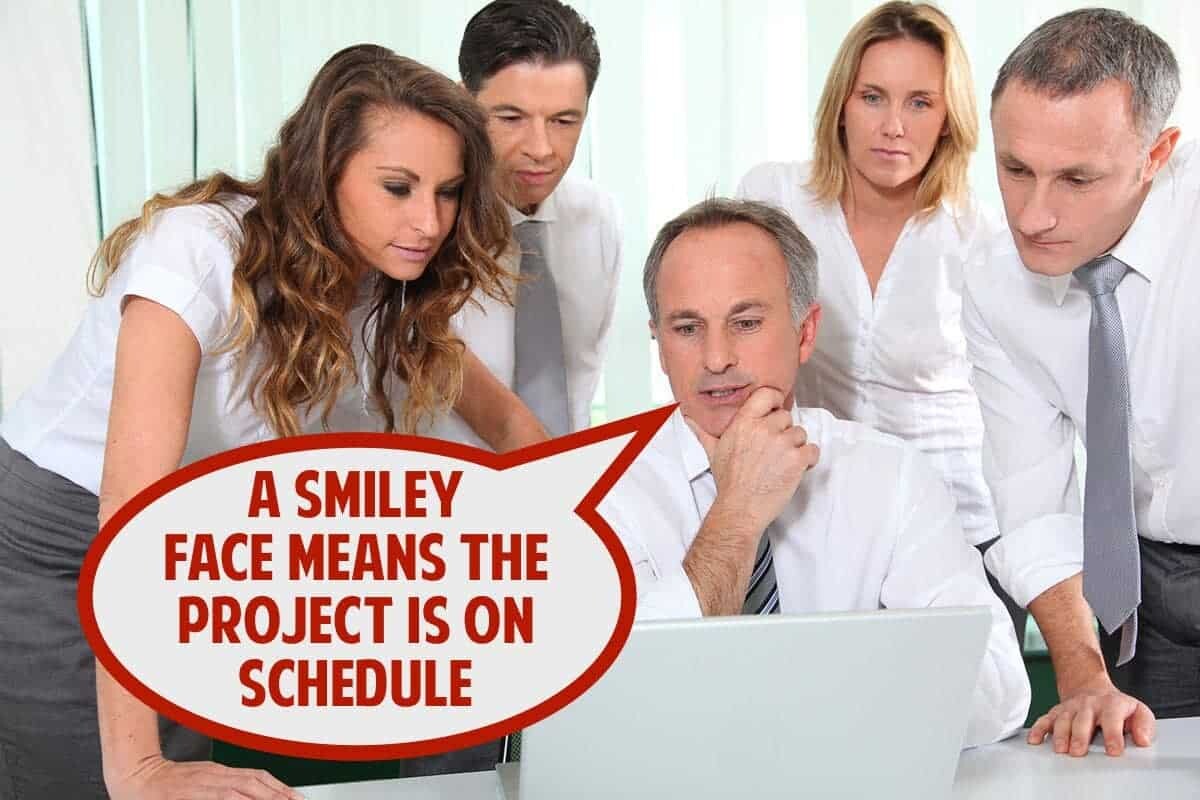 A group of five office workers, two women and three men, are gathered around a laptop. One man, seated, looks at the screen while the others stand and also focus on the laptop. A speech bubble near the seated man says, "A smiley face means the project is on schedule.