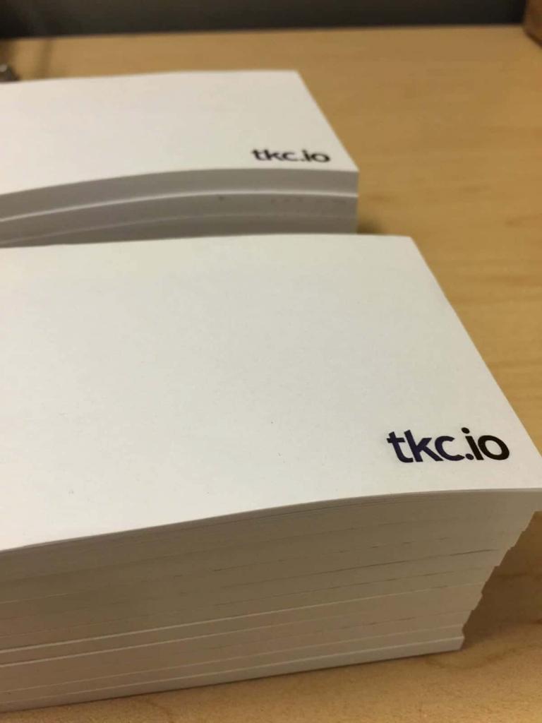Stacks of POST-IT notes with the text "tkc.io" printed in the top right corner are arranged on a wooden surface.