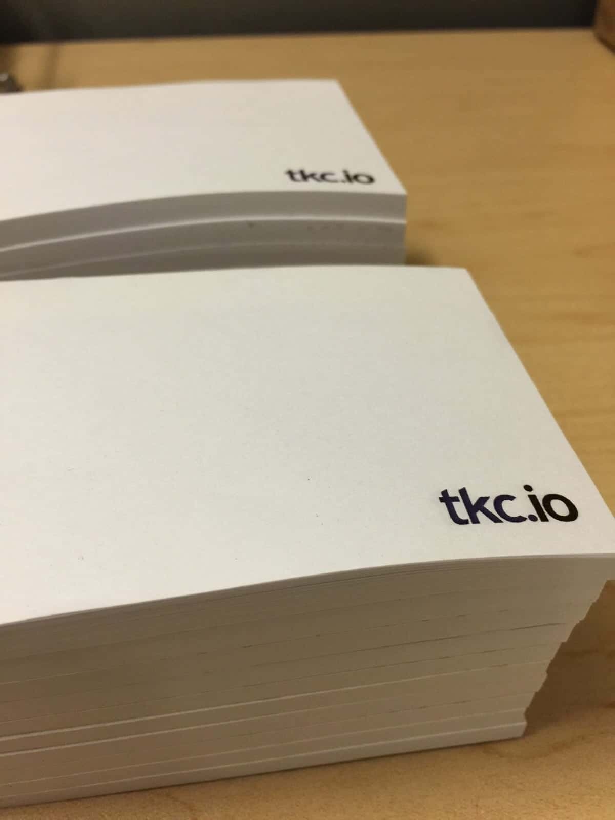 Stacks of POST-IT notes with the text "tkc.io" printed in the top right corner are arranged on a wooden surface.