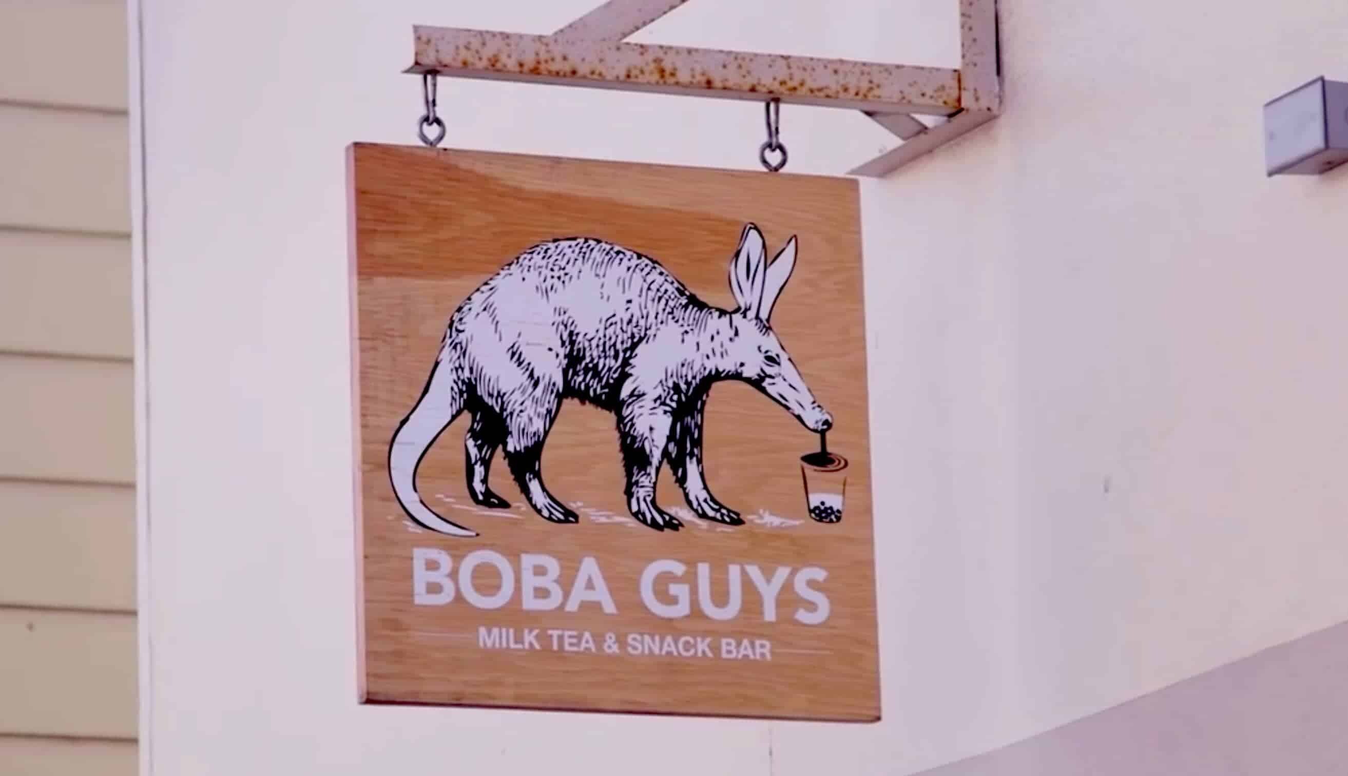 A wooden sign for "BOBA GUYS Milk Tea & Snack Bar" hangs outside, featuring a black-and-white illustration of an aardvark drinking from a cup with a straw—sure to catch the eye of any tech MSP managed consultant passing by.
