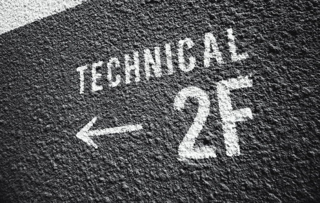 A textured black wall features white, stenciled text. The text reads "TECHNICAL" above an arrow pointing left, and "2F" beneath it. The surface appears rough and the text is stylized in a bold, legible font.