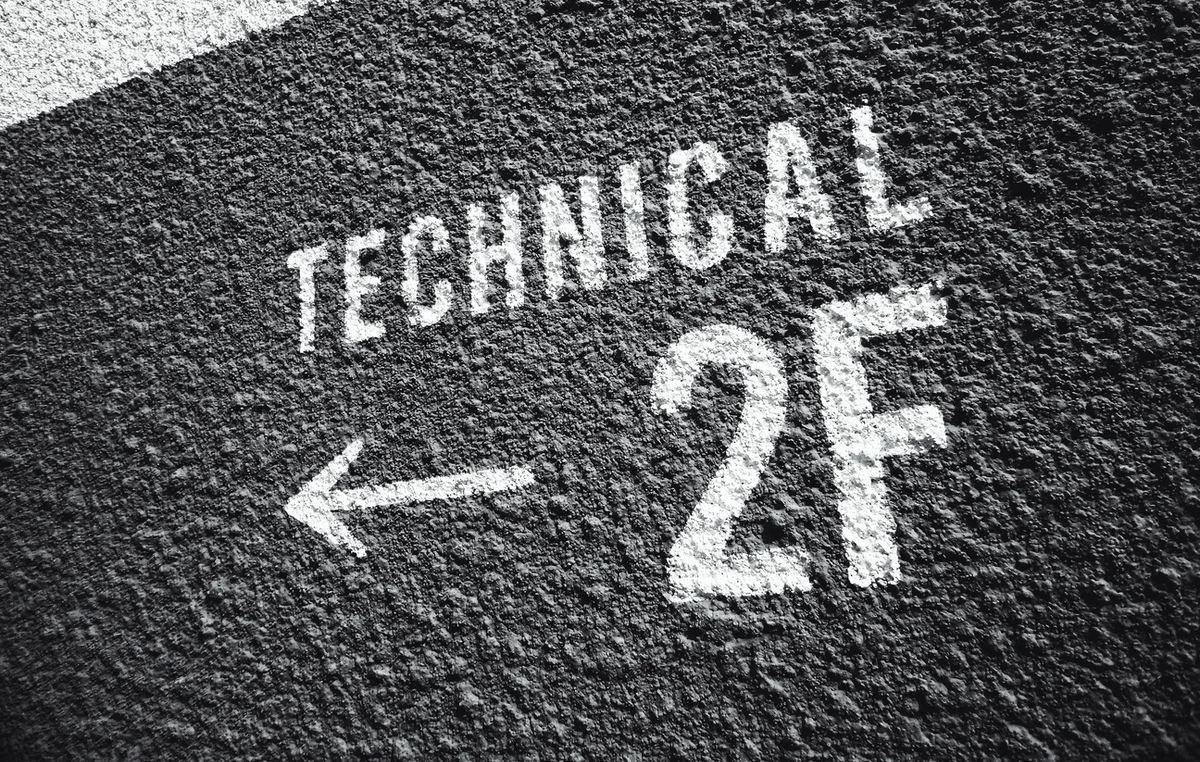 A textured black wall features white, stenciled text. The text reads "TECHNICAL" above an arrow pointing left, and "2F" beneath it. The surface appears rough and the text is stylized in a bold, legible font.