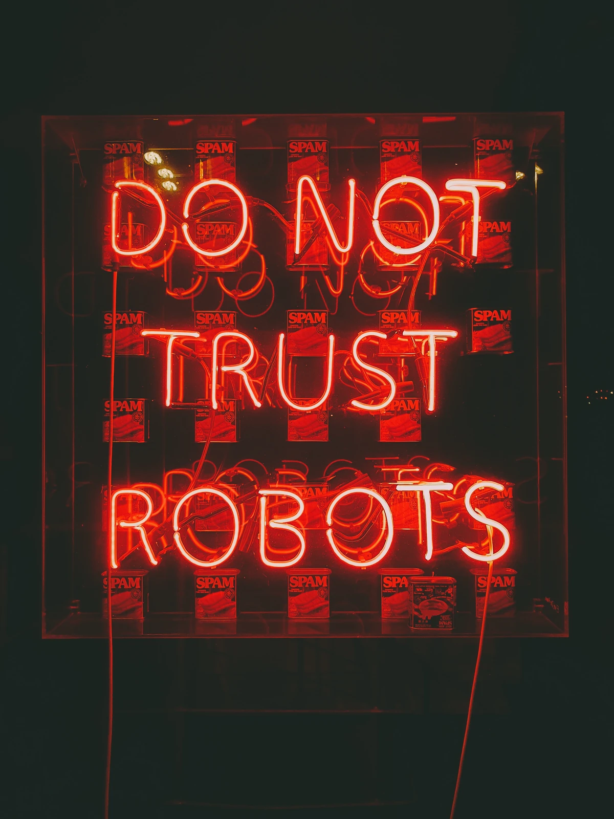 A bright neon sign in red letters reads "DO NOT TRUST ROBOTS" against a dark background. Behind the sign are several cans of SPAM, adding a quirky element to the scene.